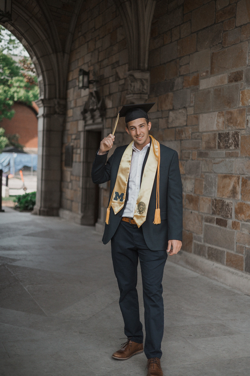 A graduate in a cap standing beneath a stone archway
