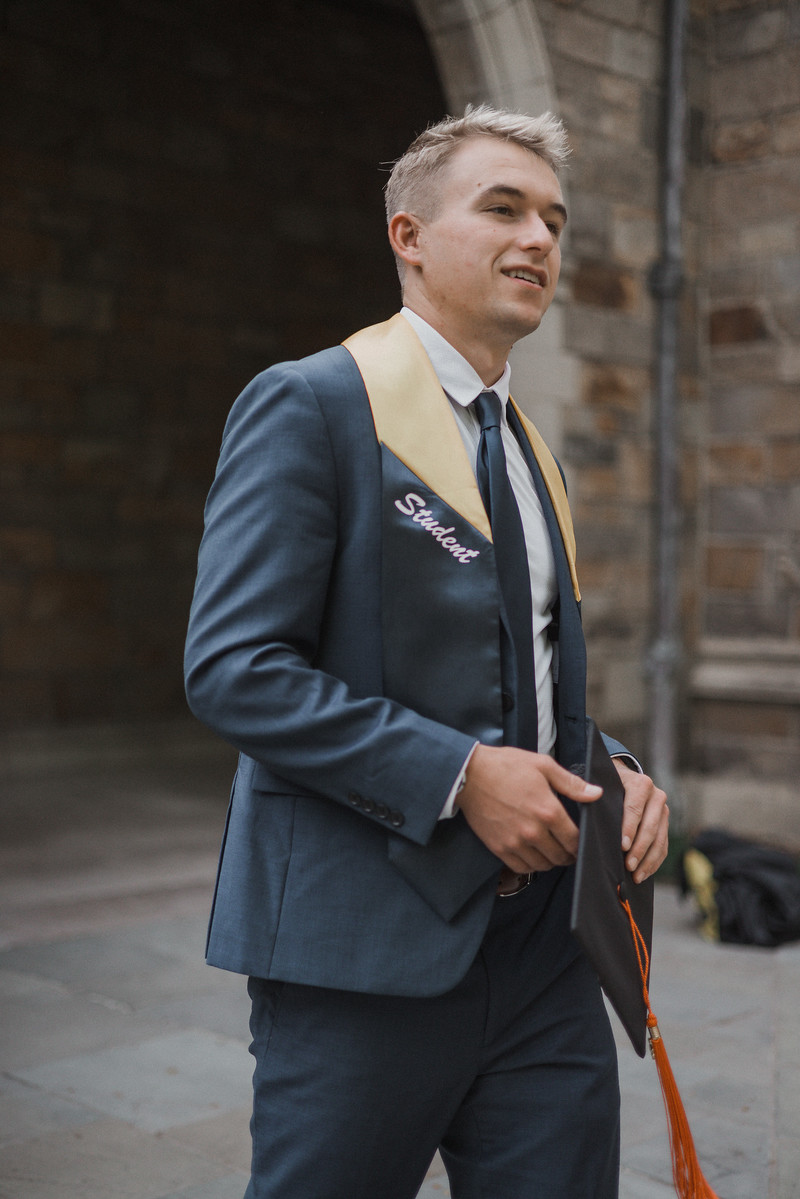 A graduate in a navy suit looking away from the camera
