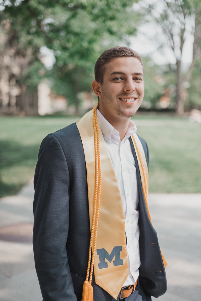 A smiling graduate wearing a dark suit and a gold stole