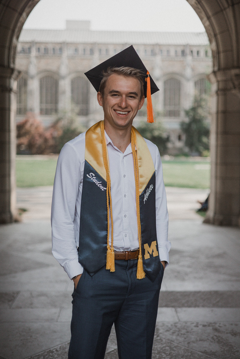 A graduate smiling beneath a stone archway