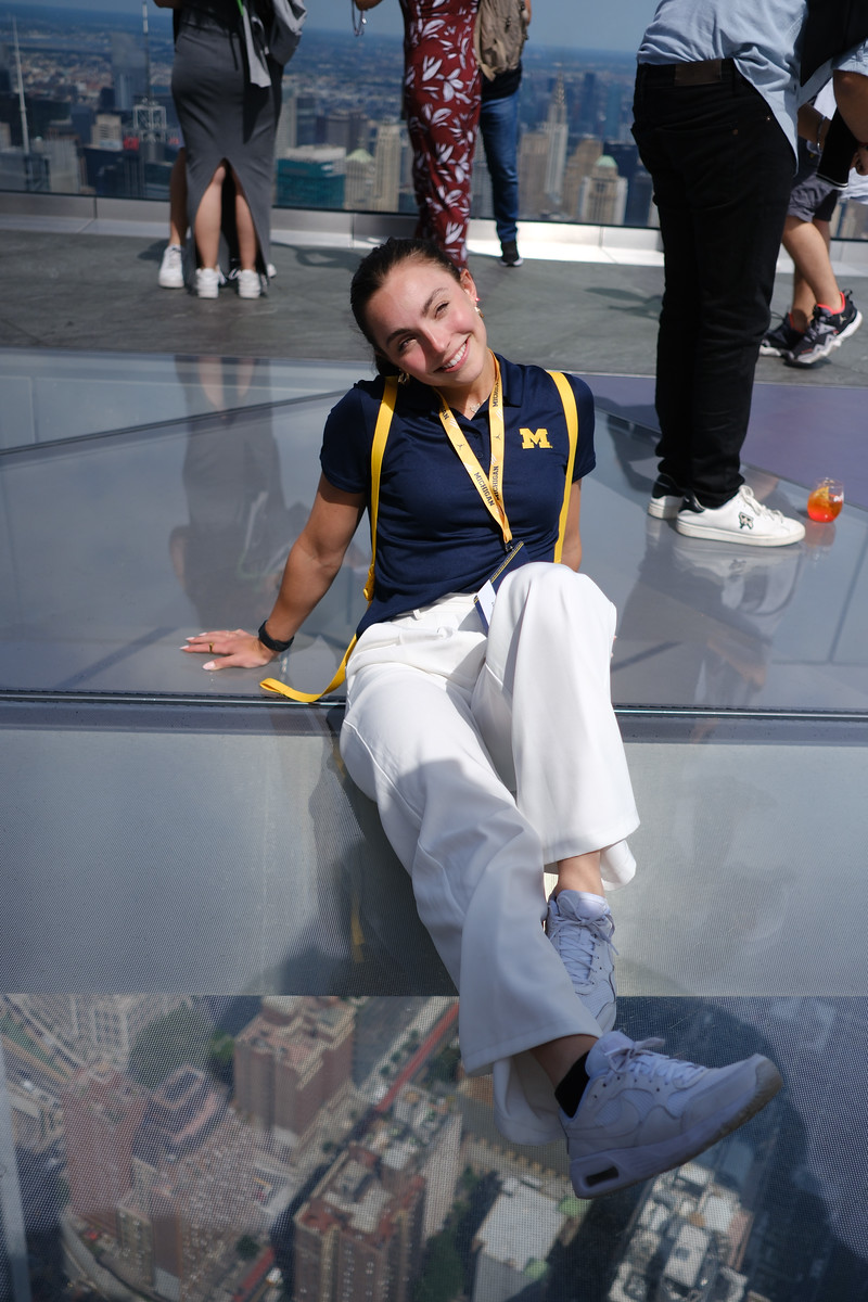 A woman sitting on a glass observation deck above the city