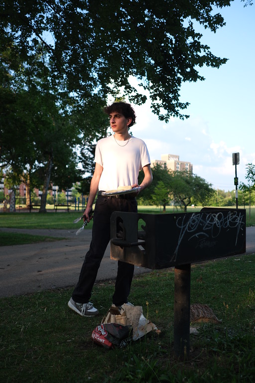 A person in a white shirt standing beneath a tree in a park
